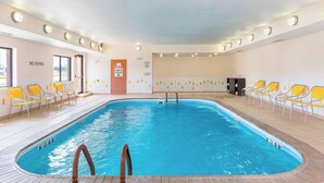 Une piscine intérieure à l’eau claire, entourée de chaises jaunes et dotée d’un sol carrelé.