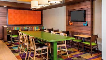 A conference room with a large green table, multiple chairs, a television, and a colorful carpet.