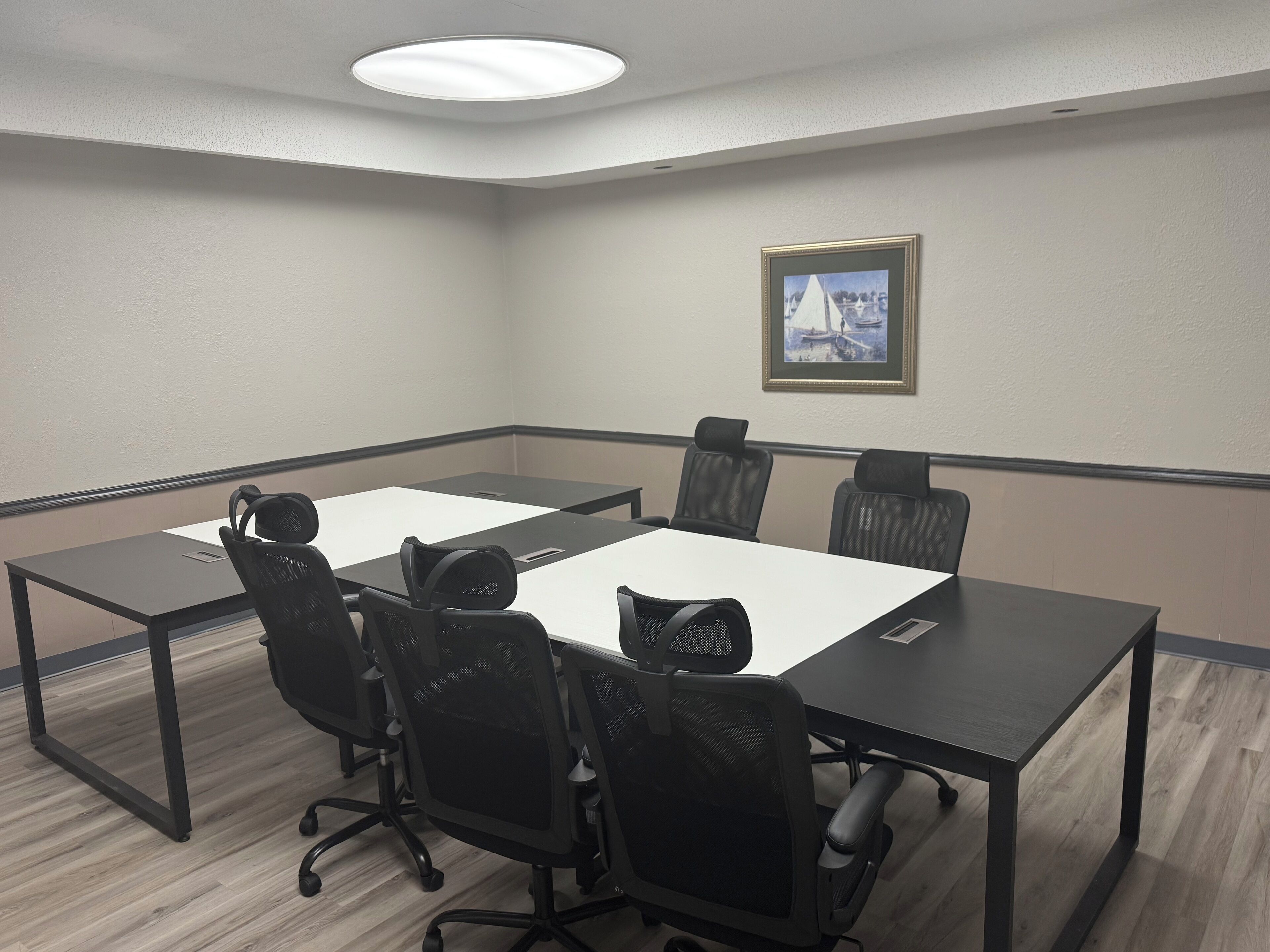 A conference room with a large table, six chairs, and a framed picture on the wall.