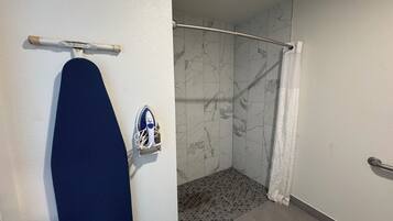 A bathroom with a shower, a towel rack with a blue towel, and a wall-mounted iron.