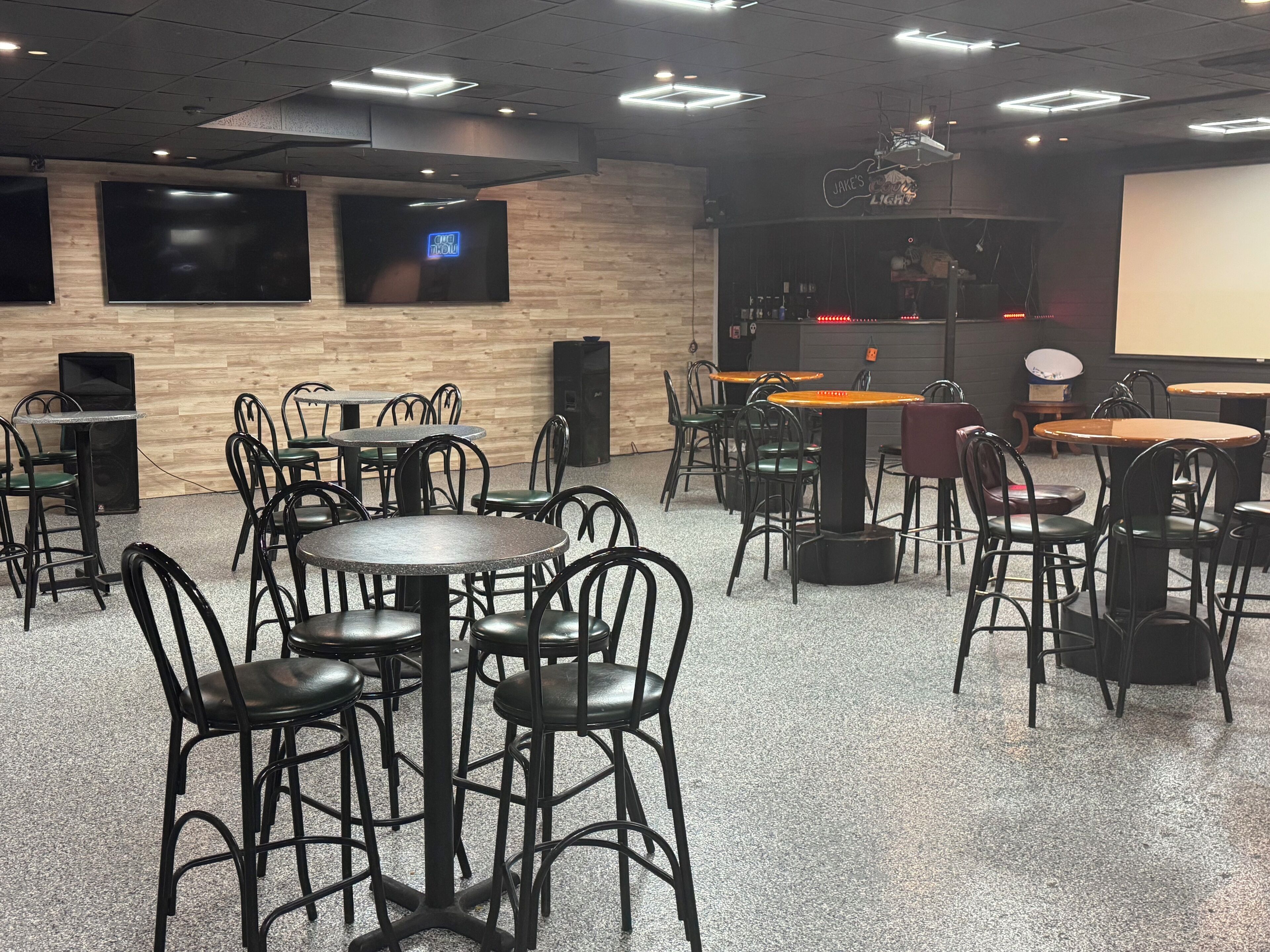 Un restaurant doté de nombreuses tables et chaises, d’une scène avec un écran et d’un espace bar.