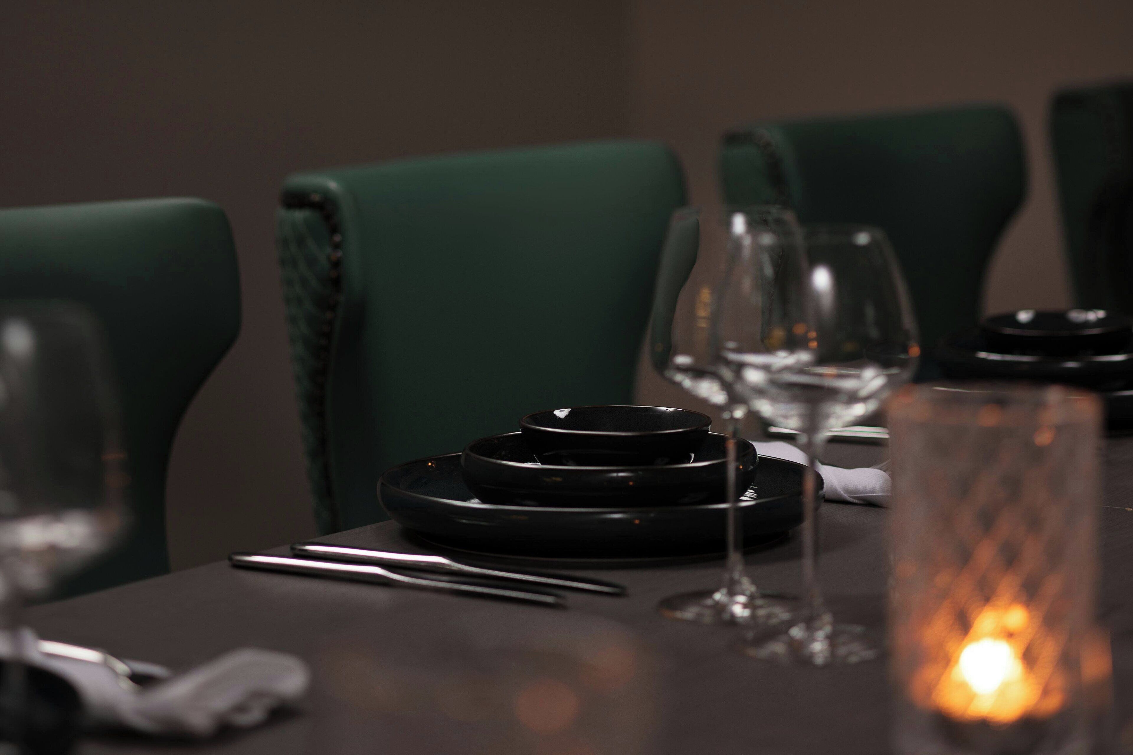A dining table set with black plates, silverware, and wine glasses, accompanied by a candle.