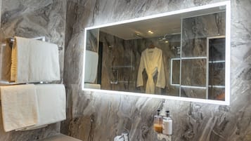 A bathroom with marble walls, a large mirror, a sink, and two towels hanging on a rack.