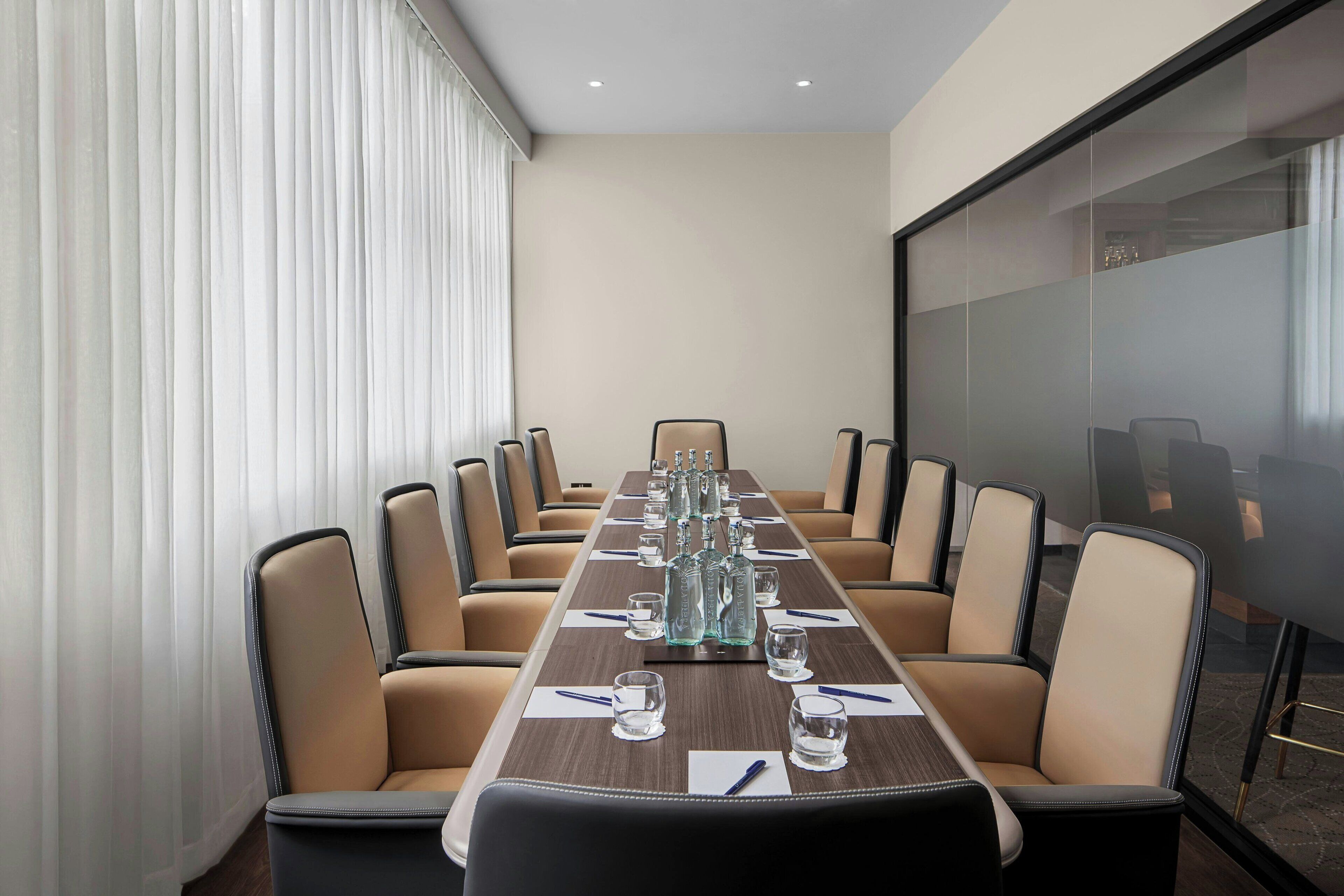 A conference room with a long table, beige chairs, and a glass partition.