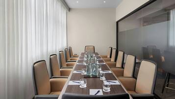 A conference room with a long table, beige chairs, and a glass partition.
