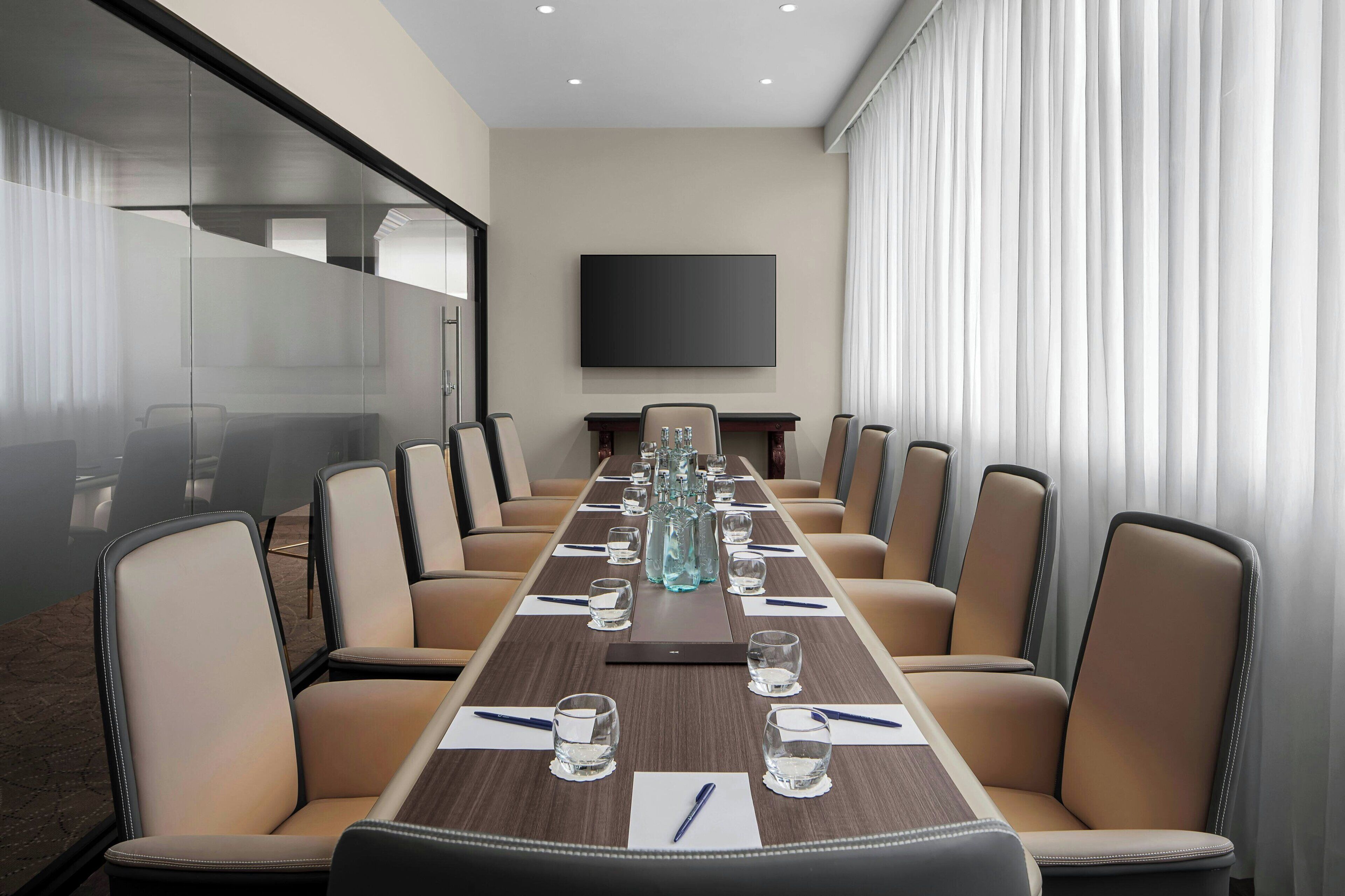 A conference room with a long table, beige chairs, and a flat-screen TV on the wall.