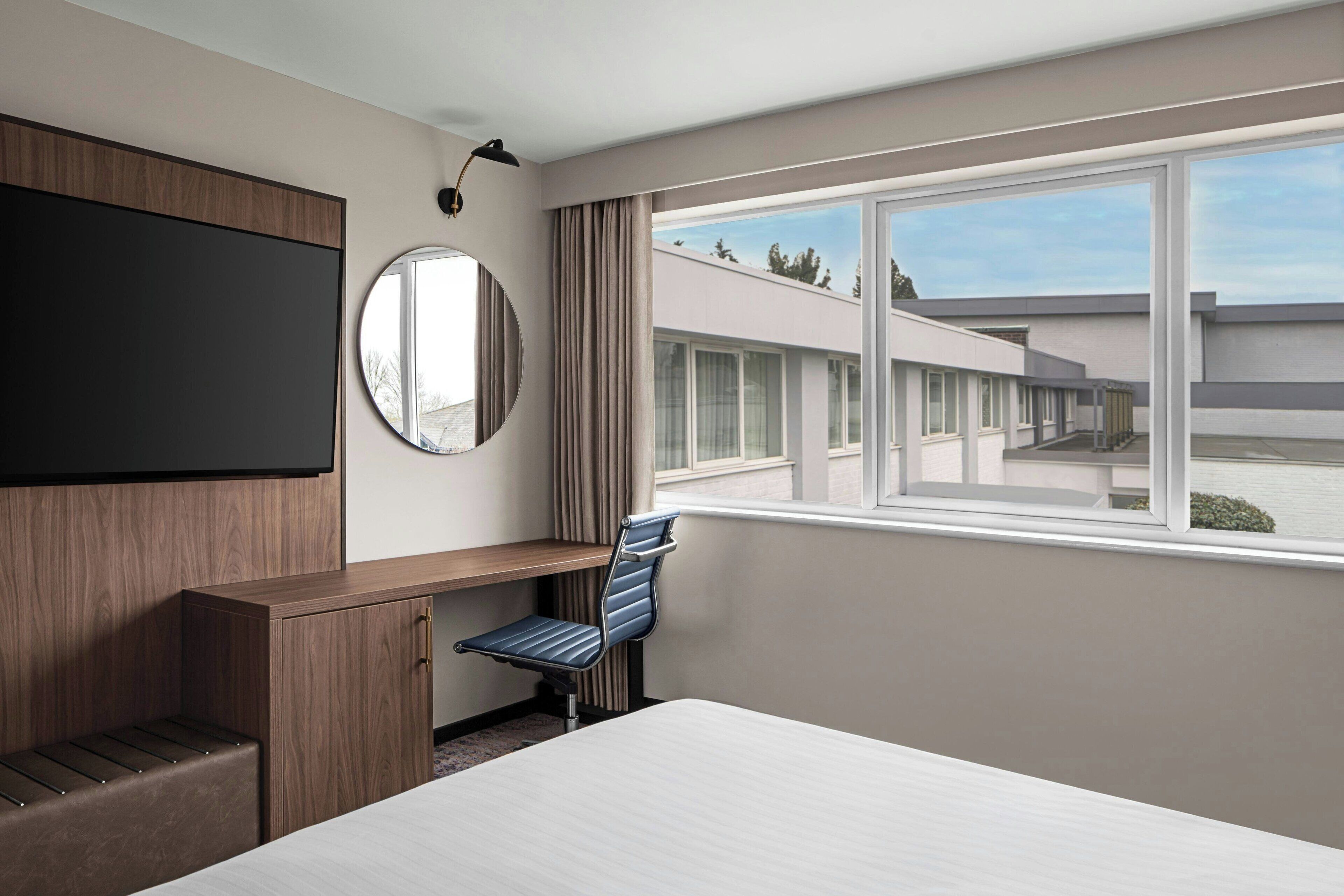 Camera d'albergo con un letto, una scrivania con una sedia, una TV a parete e un'ampia finestra che dà sull'esterno dell'edificio.