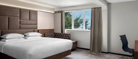 A modern hotel room with a large bed, a desk, and a window with curtains.