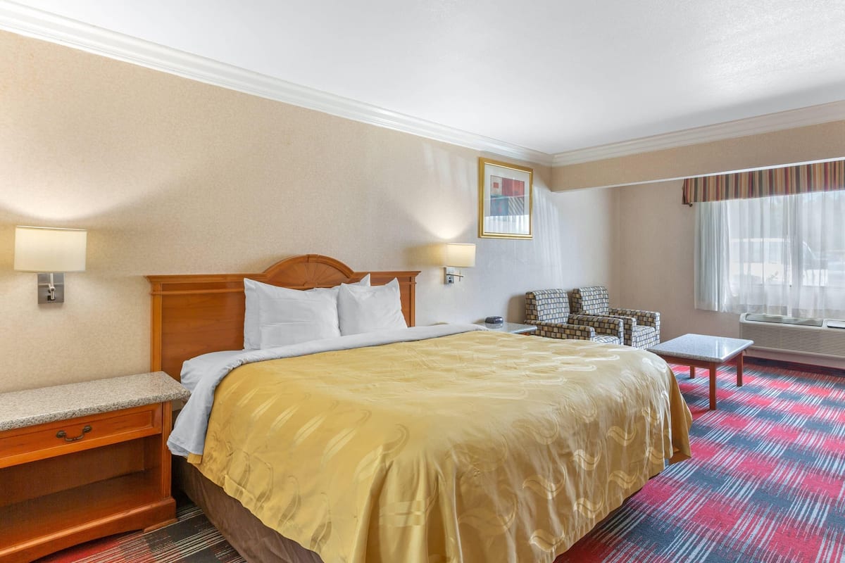Habitación de hotel con una cama grande, un escritorio, una silla y un ventanal con cortinas.