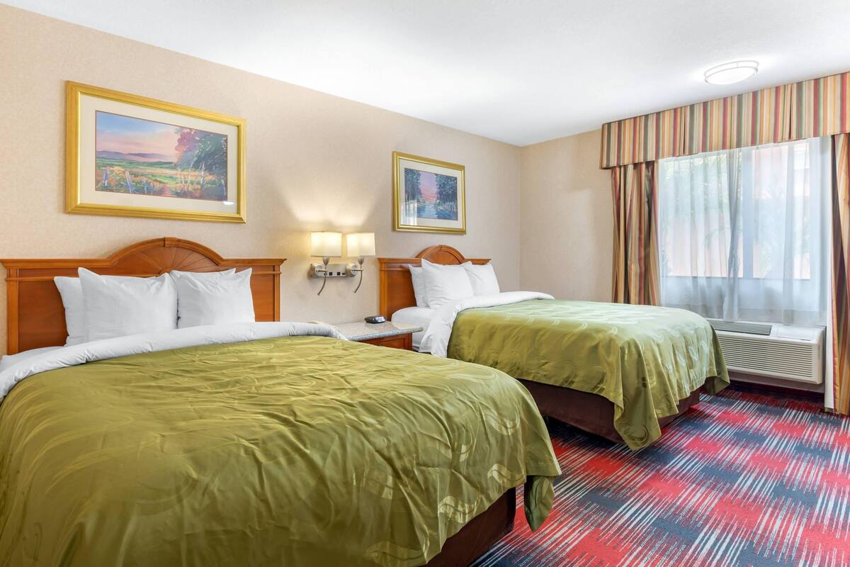 Una habitación de hotel con dos camas, un ventanal con cortinas y dos lámparas fijadas a la pared.