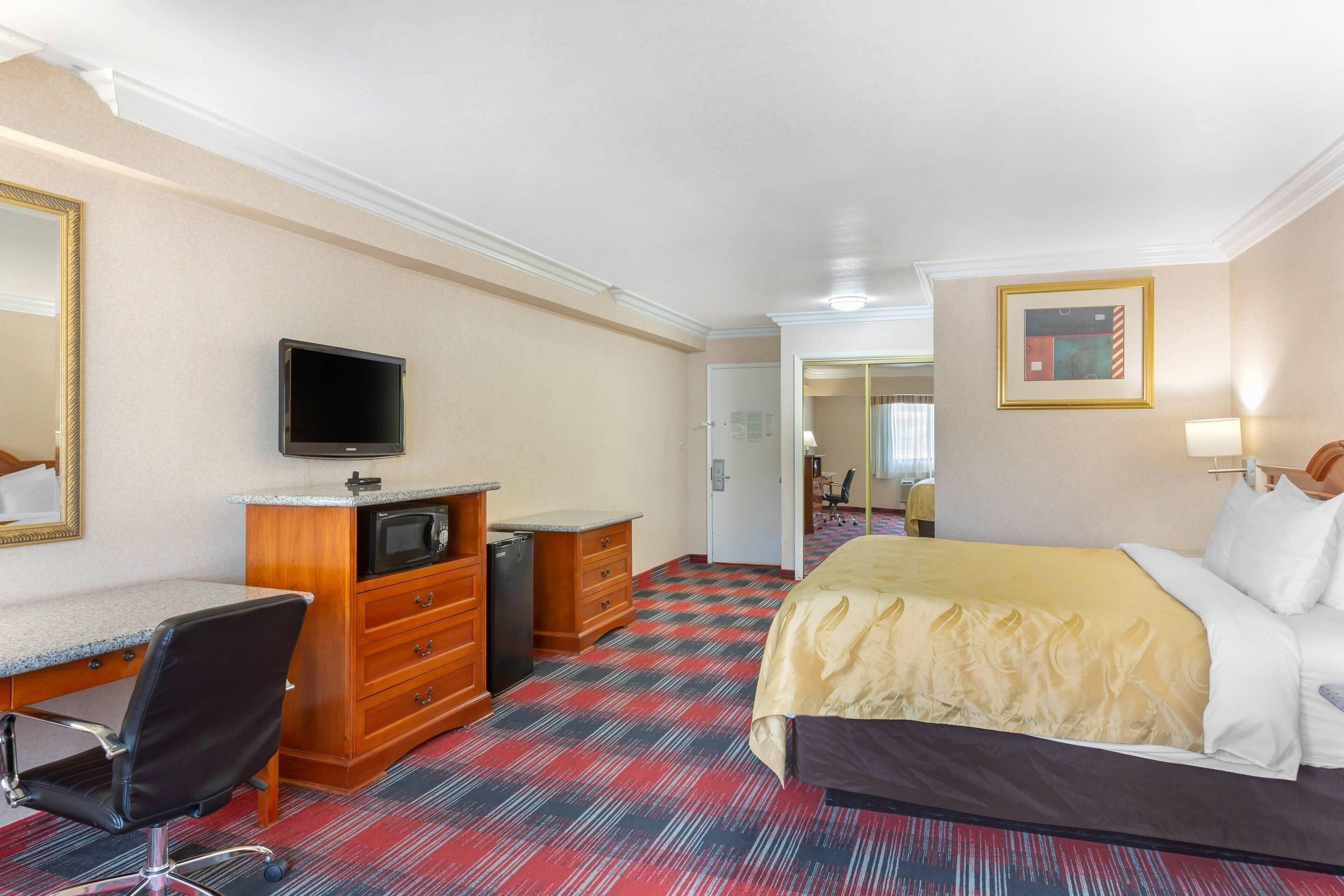 A hotel room with a bed, desk, chair, television, and a door leading to another room.