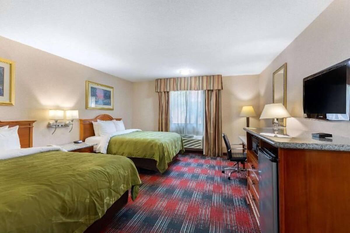 A hotel room with two beds, a desk with a TV, a chair, and a window with curtains.
