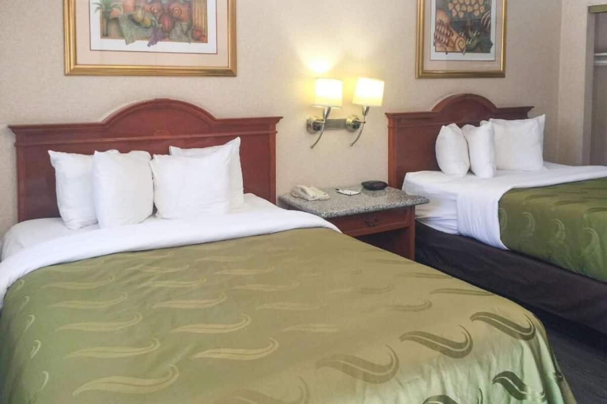 Habitación de hotel con dos camas, cada una con cabecero de madera, mesita de noche con teléfono y lámparas fijadas a la pared.