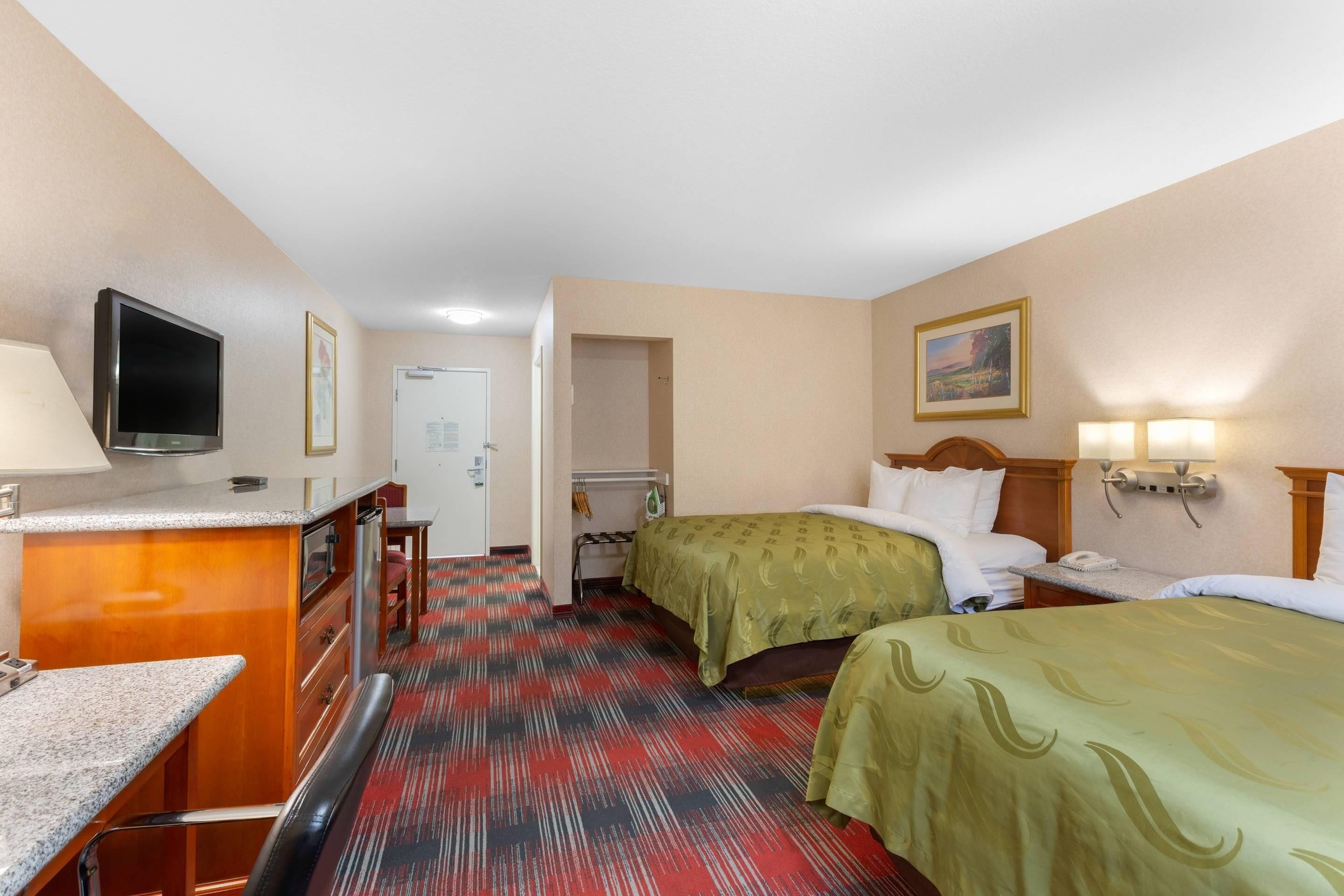 Una habitación de hotel con cama, mesita de noche, lámpara y televisor sobre un escritorio.