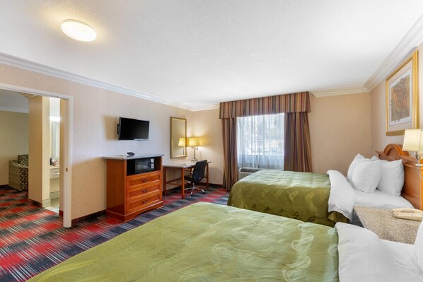 A hotel room with two beds, a desk, a TV, and a bathroom visible through an open door.