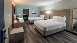 Quarto de hotel com duas camas, uma escrivaninha com abajur, um espelho e piso de madeira.