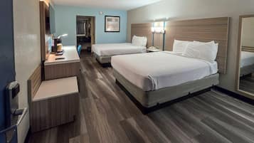 Habitación de hotel con dos camas, un escritorio con lámpara, un espejo y piso de madera.