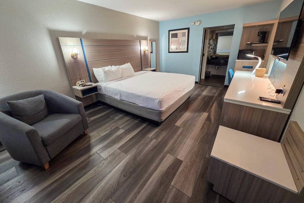 A hotel room with a bed, a chair, a desk, and a kitchenette.