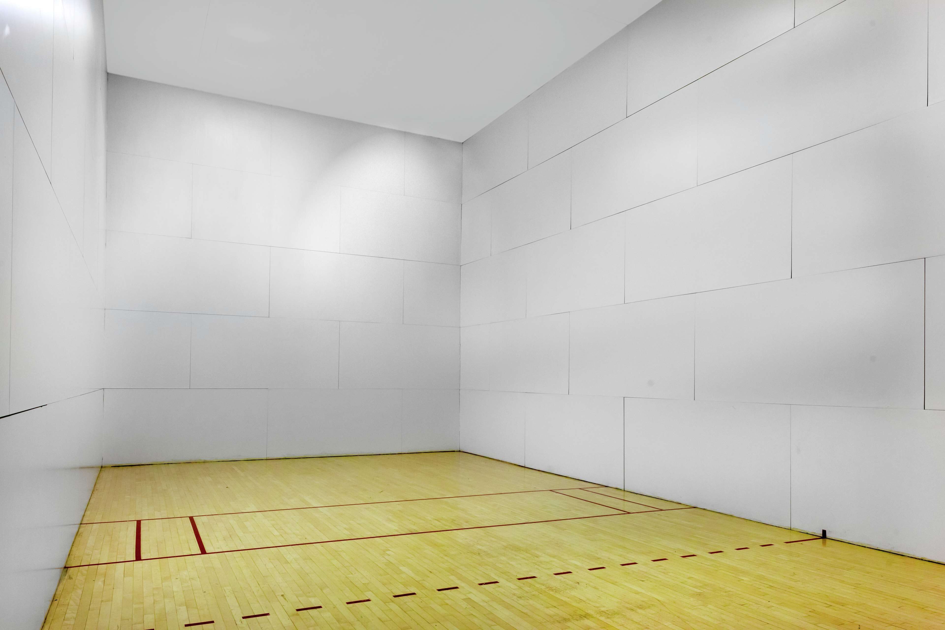 Una cancha de squash con paredes blancas y piso de madera.