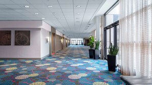Un pasillo de hotel con alfombra estampada, ventanas amplias y un banco.
