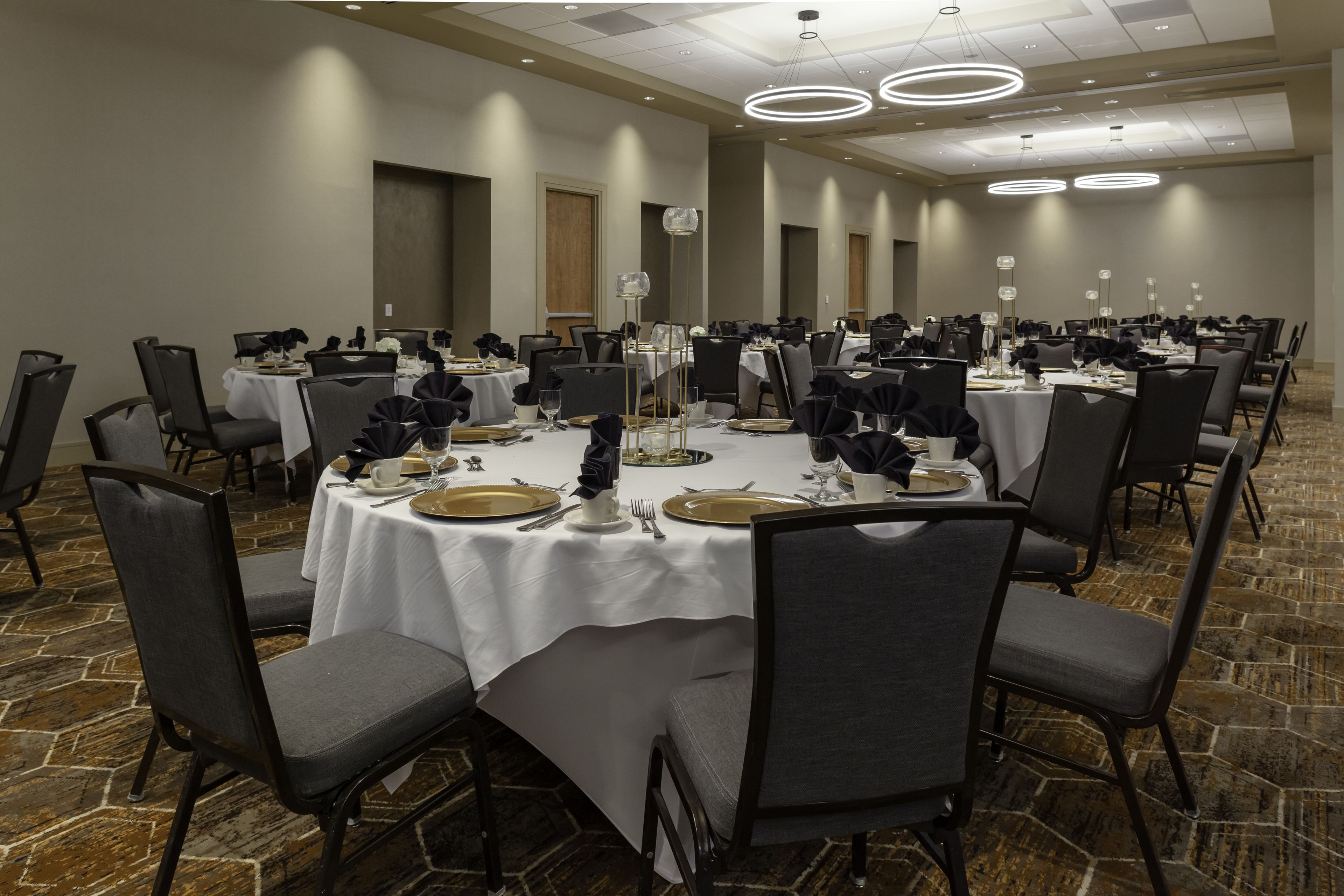 A conference room with round tables, black chairs, and white tablecloths.
