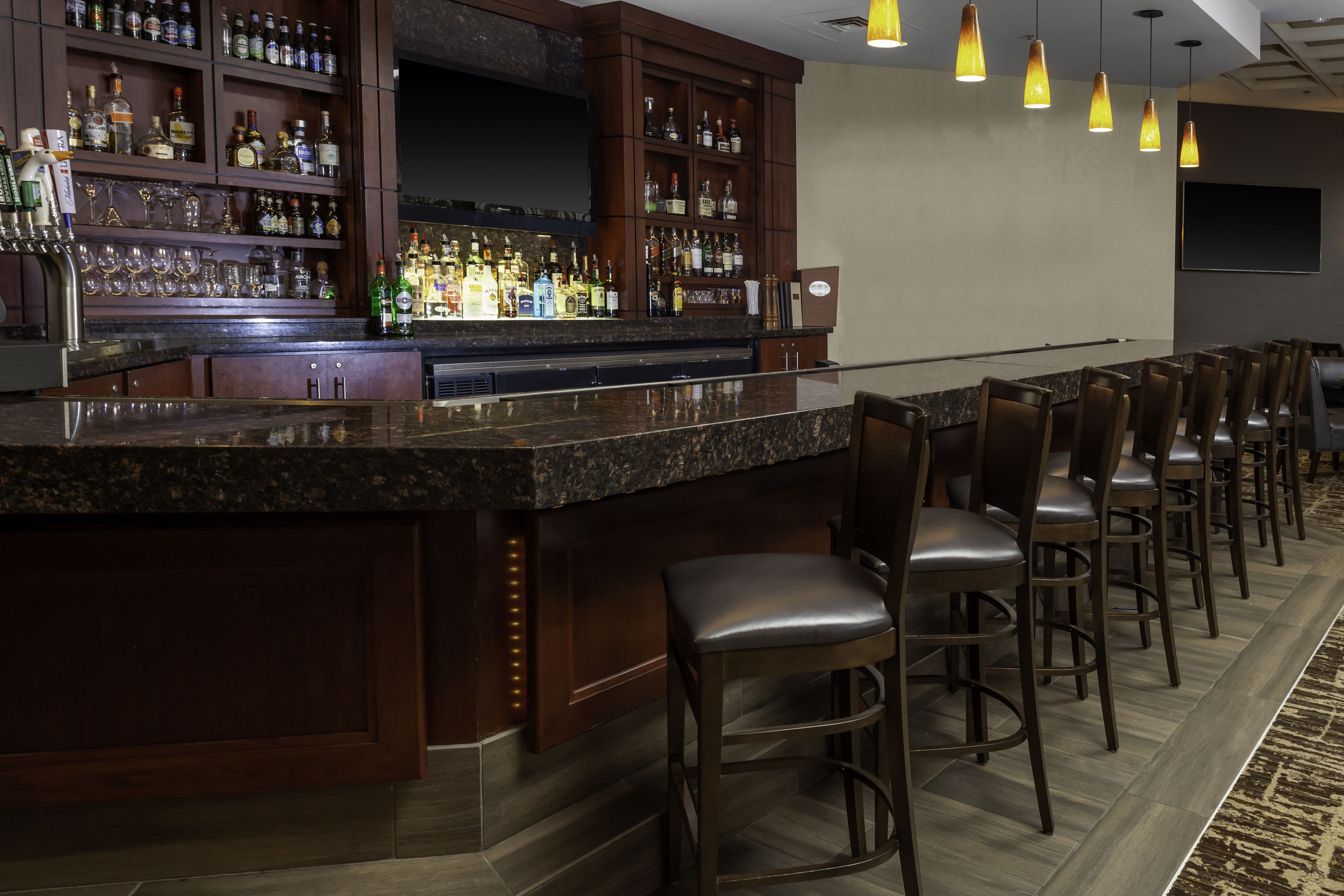 A bar area with a granite countertop, multiple bar stools, and a variety of liquor bottles.
