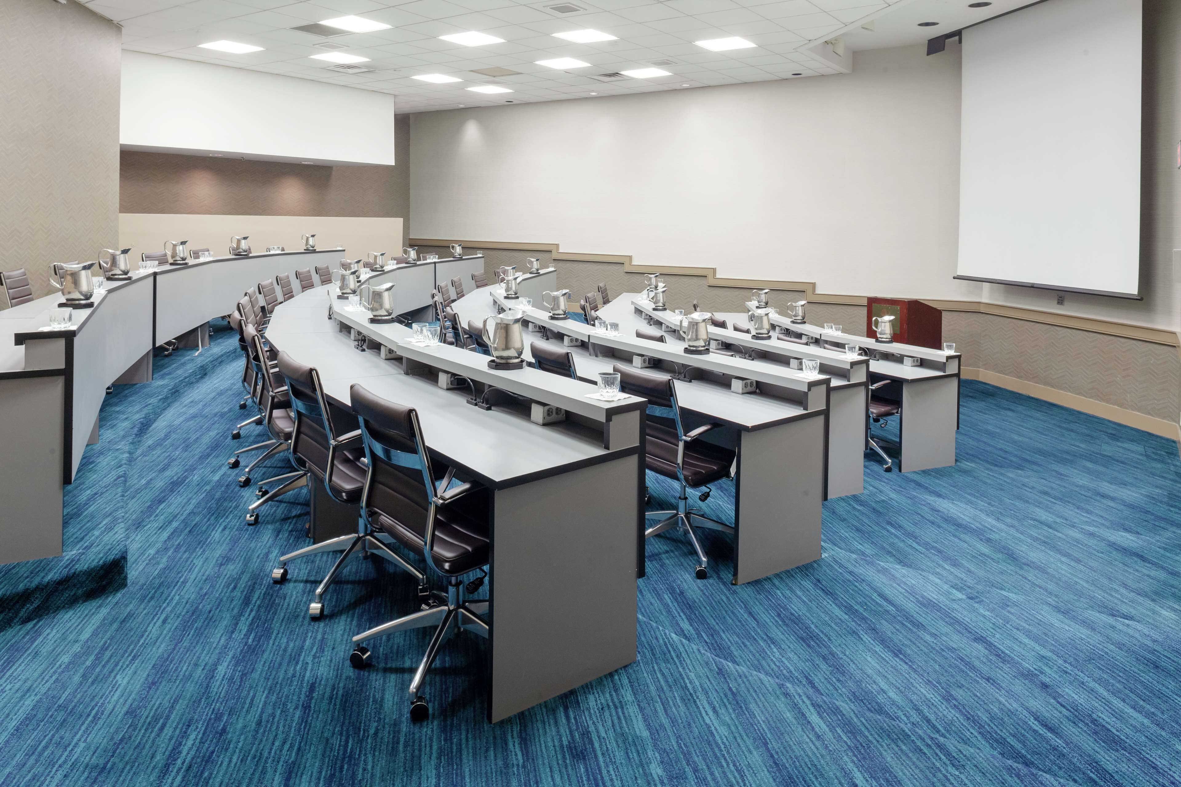 Un salón de conferencias con una mesa en forma de U, sillas y una pantalla para proyector.