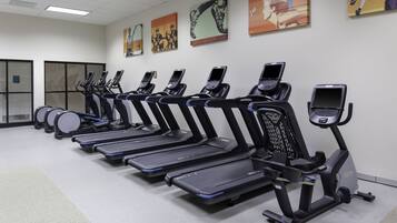 Varias bicicletas estáticas con pantallas, una cinta de correr y una máquina de remo en un gimnasio.