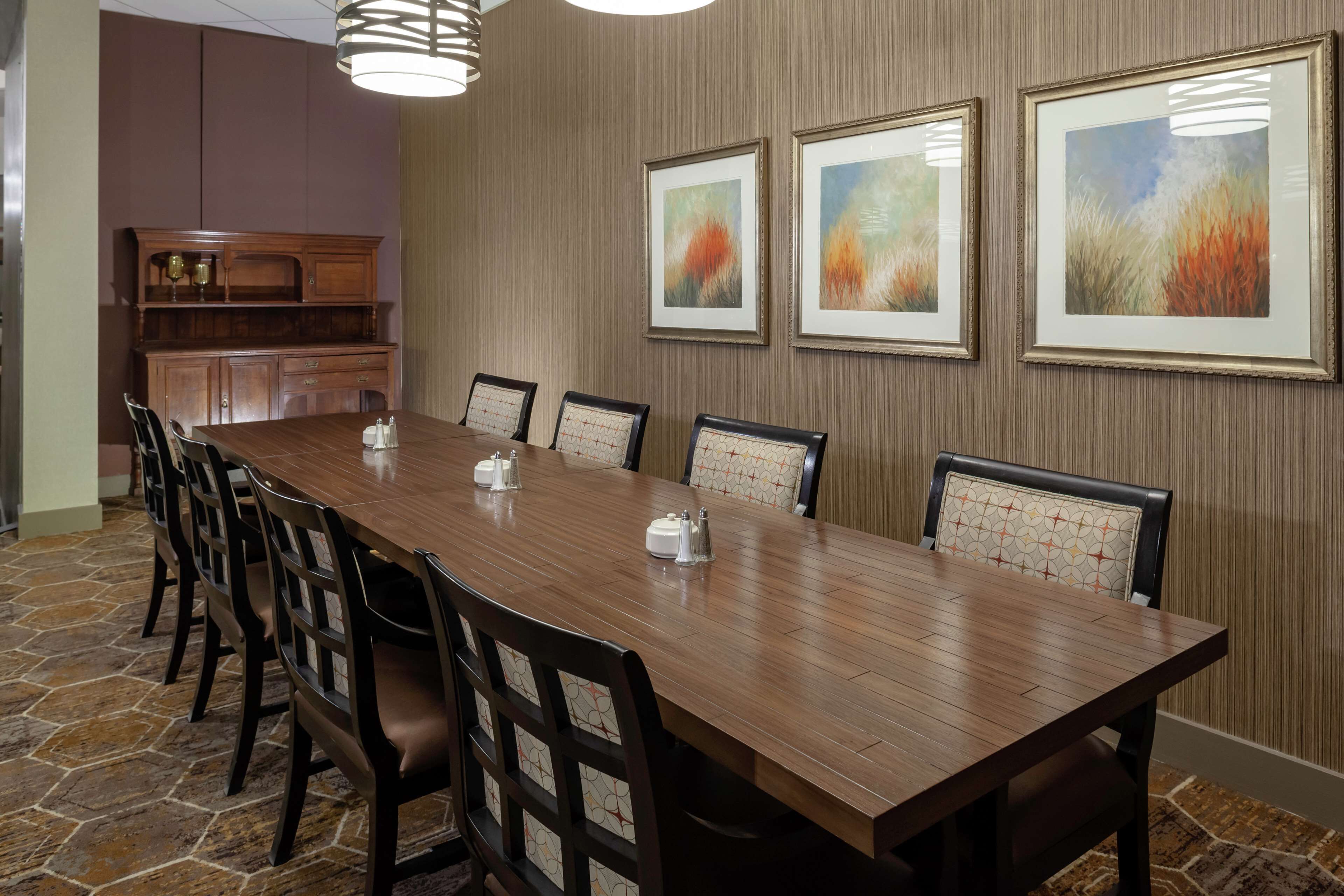 A conference room with a long wooden table, black chairs with patterned cushions, and framed artwork on the walls.