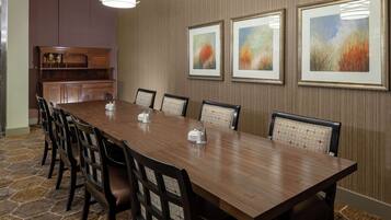 A conference room with a long wooden table, black chairs with patterned cushions, and framed artwork on the walls.