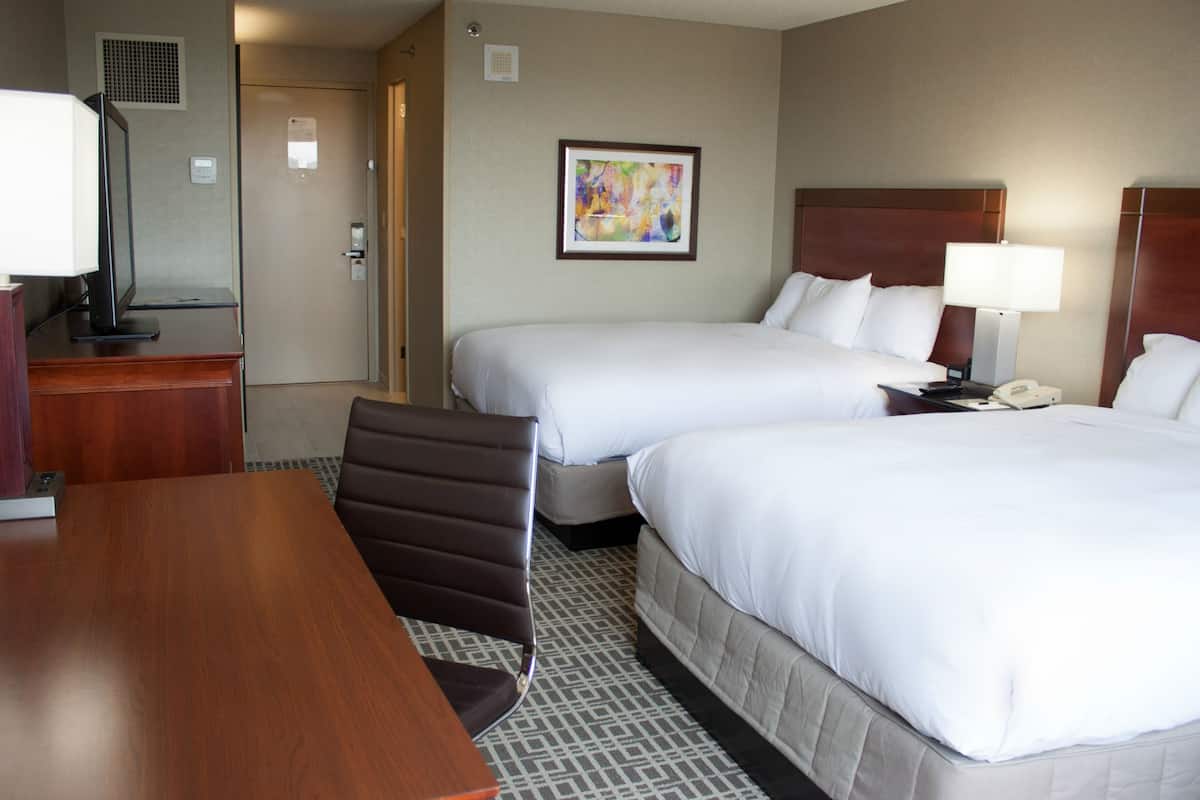 A hotel room with two beds, a desk, a chair, a desk lamp, a telephone, and a framed picture on the wall.
