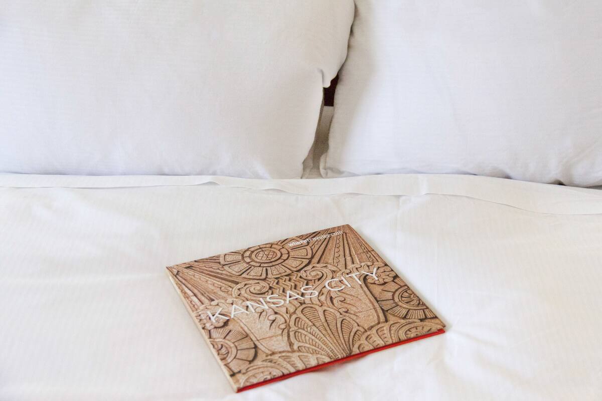 A bed with white sheets and a book titled "Kansas City" on it.