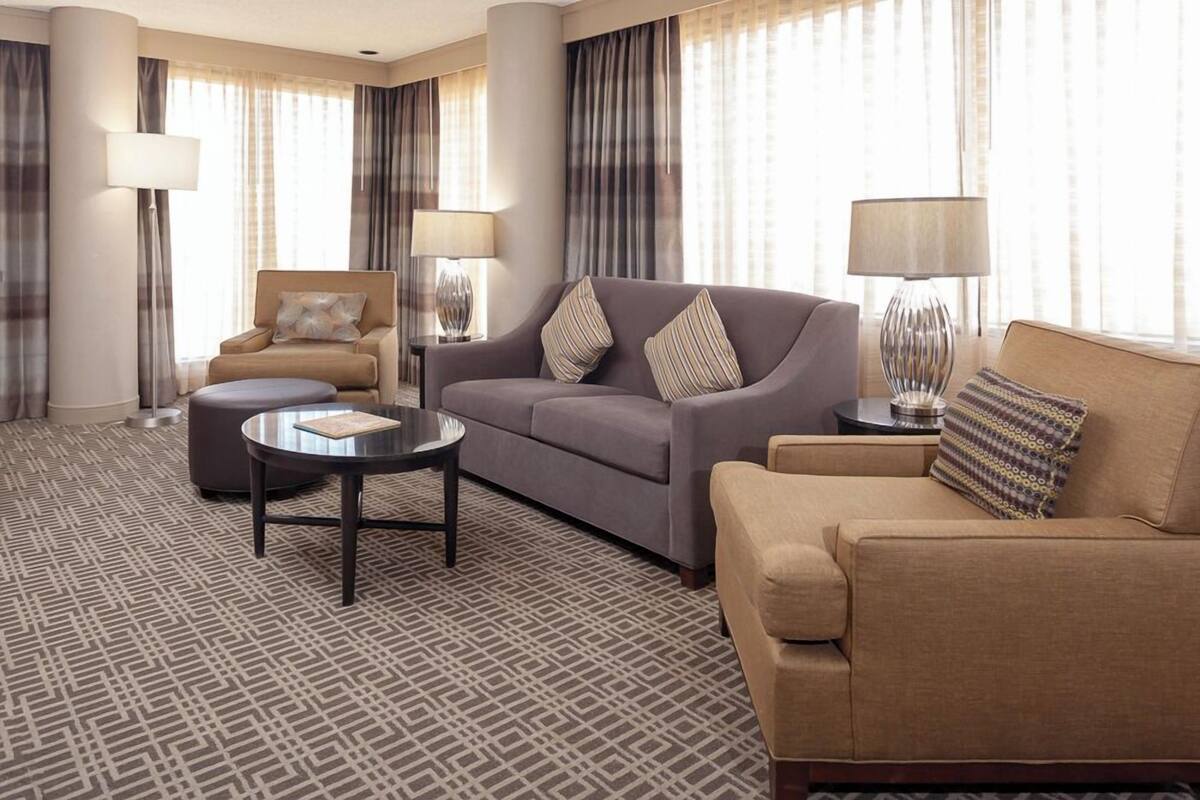 A hotel room with a patterned carpet, two sofas, a round coffee table, and two lamps.