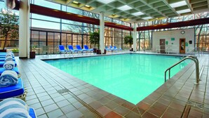 Una piscina interior con sillones reclinables azules y toallas, ventanas grandes y suelo de baldosas.