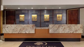 Zona de recepción de un hotel con mostrador de mármol, un logotipo en el suelo y tres paneles de pared iluminados.