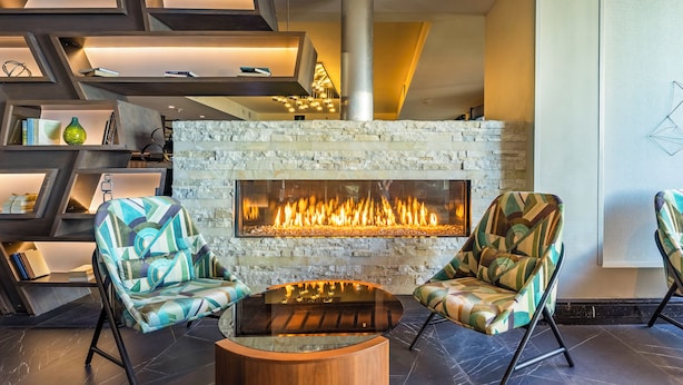 A modern lounge area with a stone fireplace, geometric shelving, and patterned armchairs.