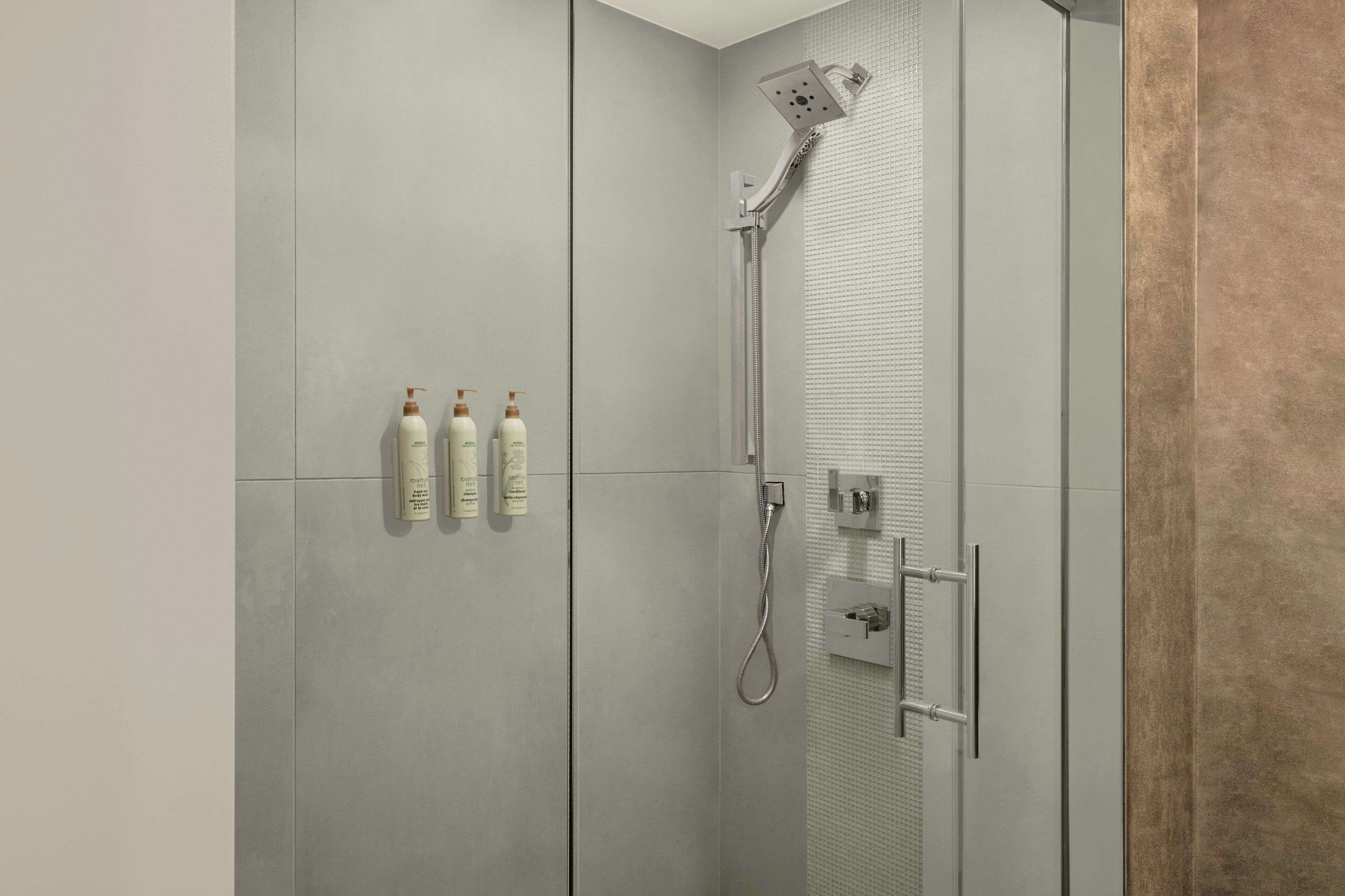 Ein moderner Duschbereich mit Handbrause, fest montierter Bedienkonsole und drei Flaschen Shampoo und Conditioner.
