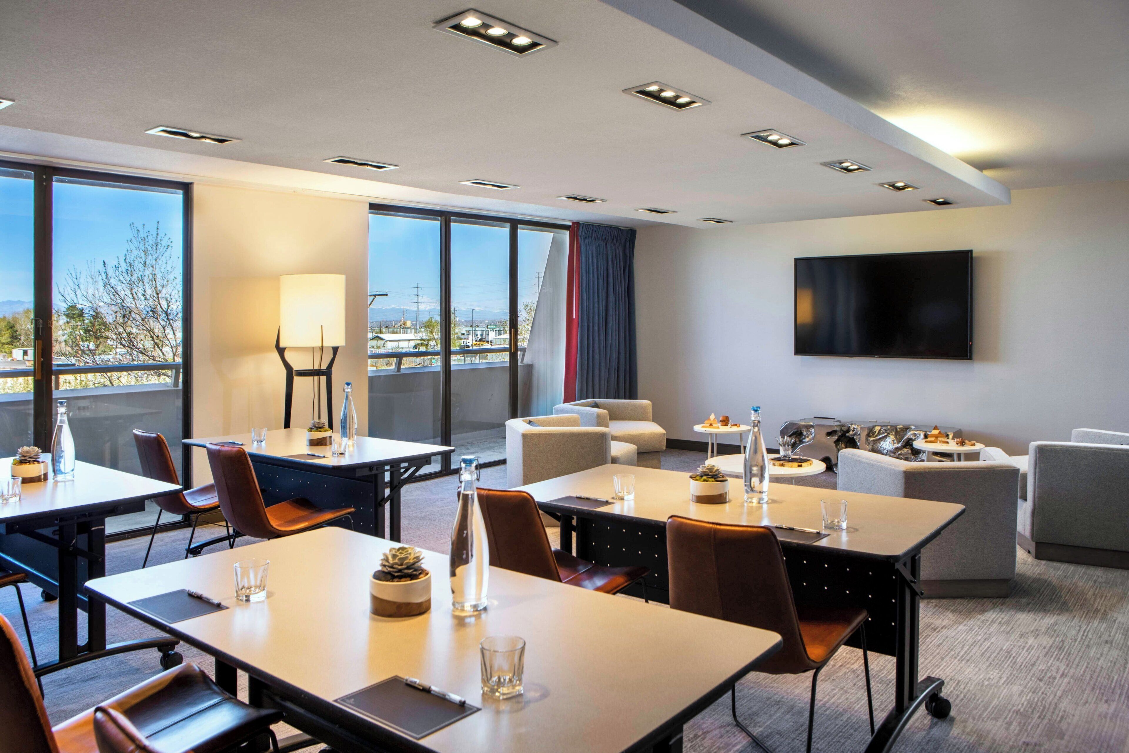 Een moderne hotelkamer met een zithoek, een bank, een flatscreen-tv en grote ramen met uitzicht op de omgeving.