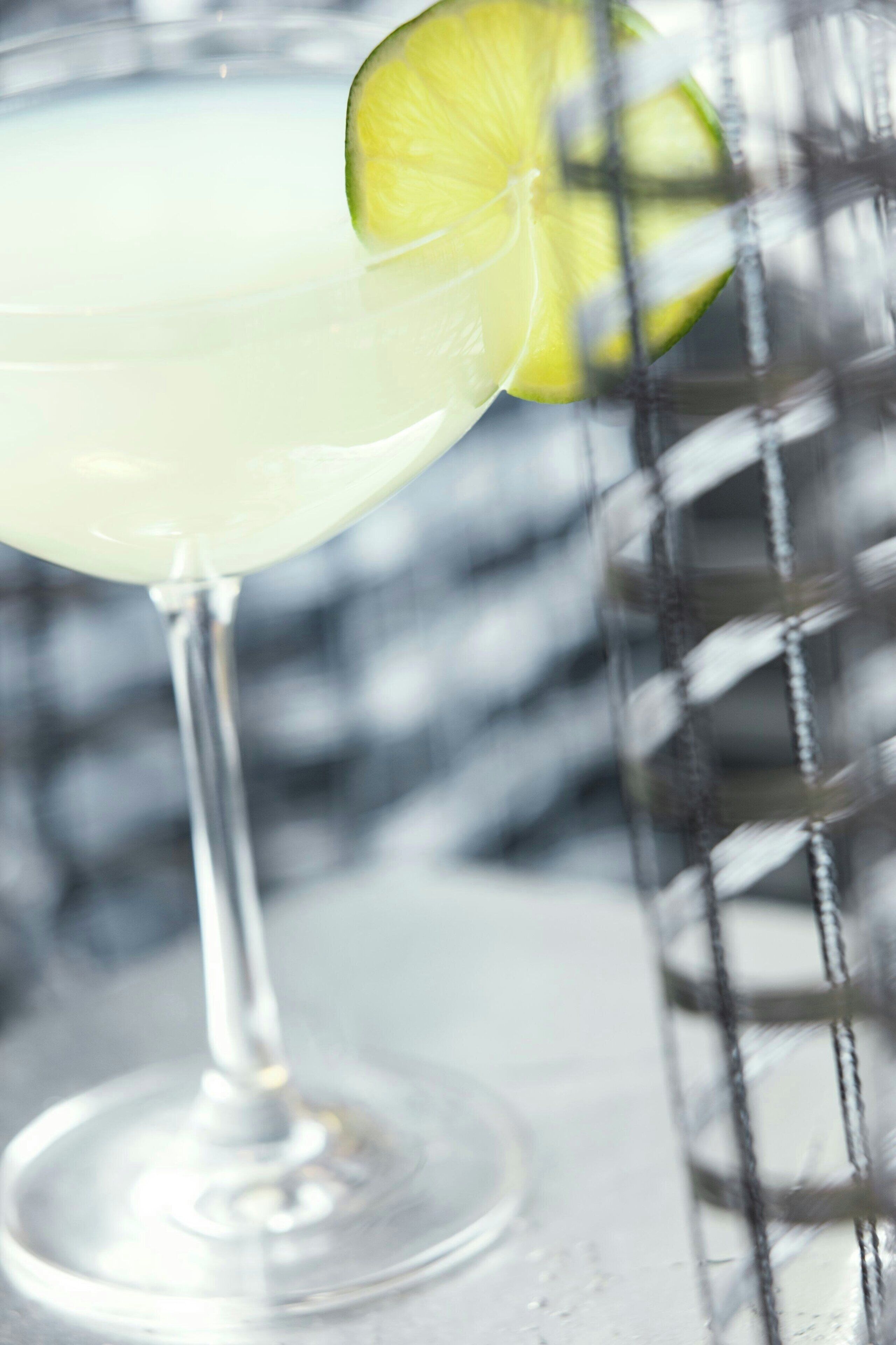 A clear glass with a lime garnish, placed on a surface with a blurred background.