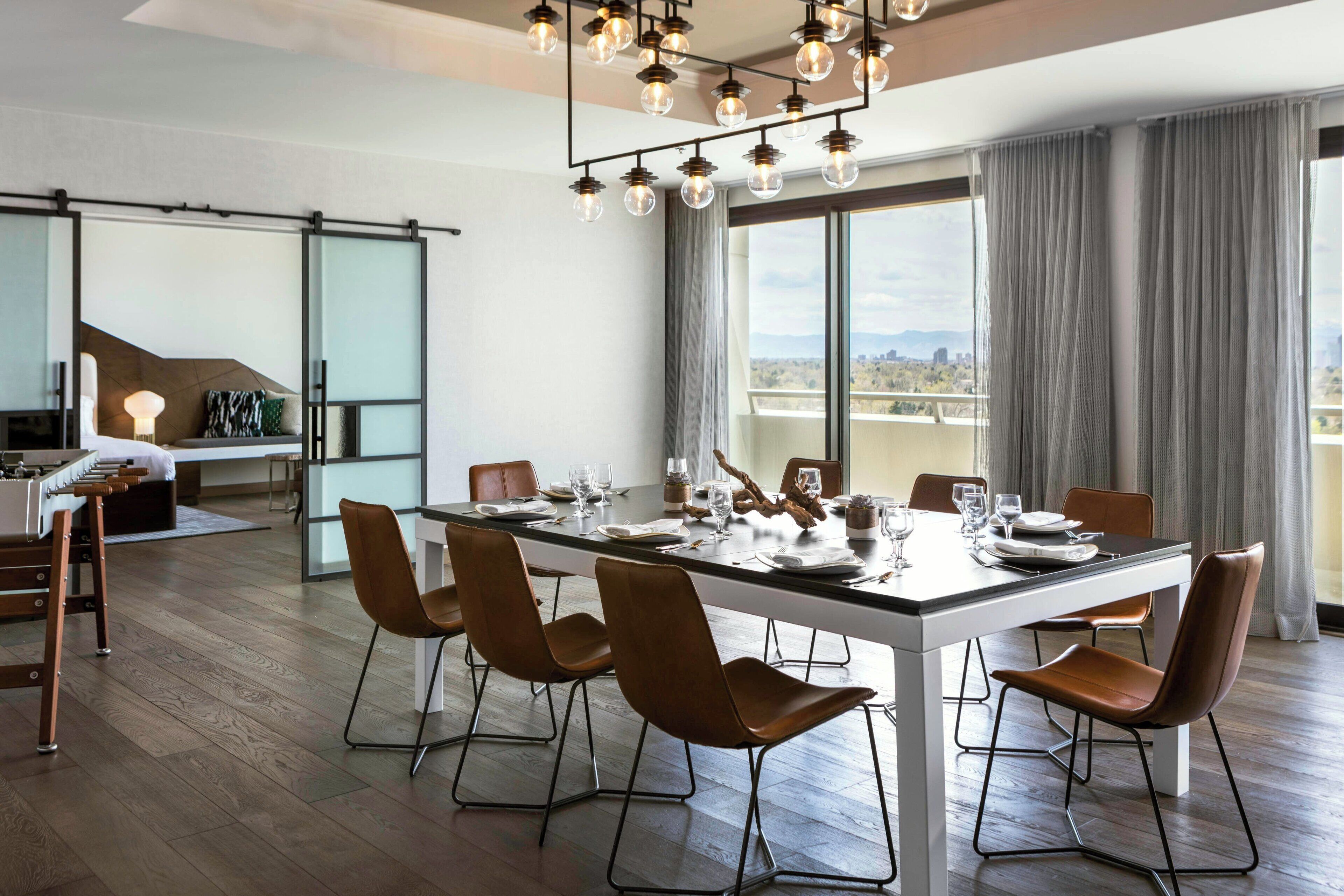 A modern dining area with a long table, six chairs, and a chandelier.