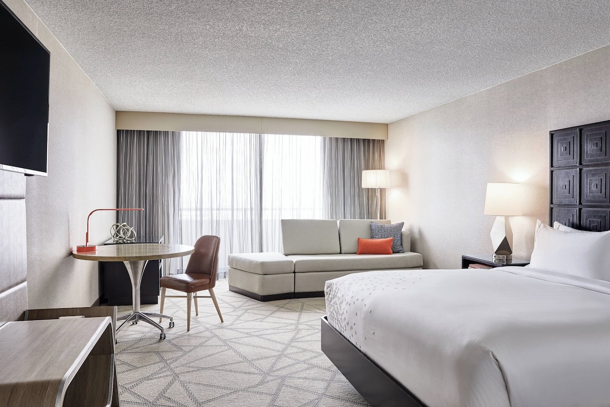 A hotel room with a bed, a desk, a chair, a sofa, and a TV.