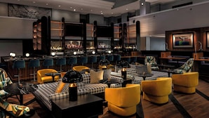 A modern bar area with checkered sofas, yellow chairs, and a bar counter with bottles.