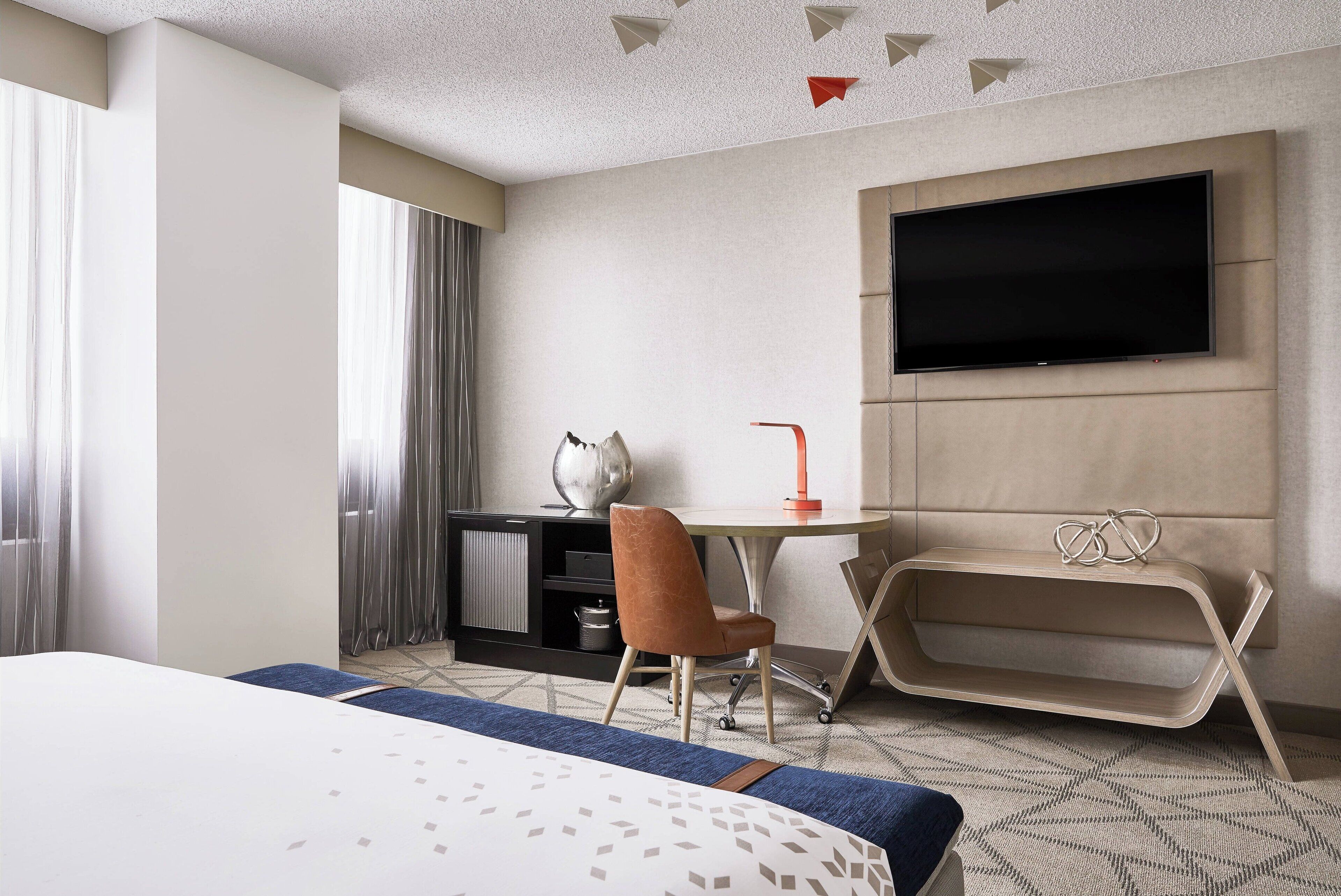 A hotel room with a bed, a desk, a chair, a television, and a small shelf.