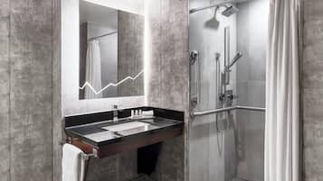 A modern bathroom with a large mirror, a black sink, a shower with a glass door, and a towel rack.