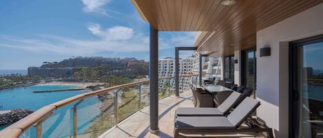 A balcony with a view of a beach and ocean, furnished with lounge chairs and a sun lounger.