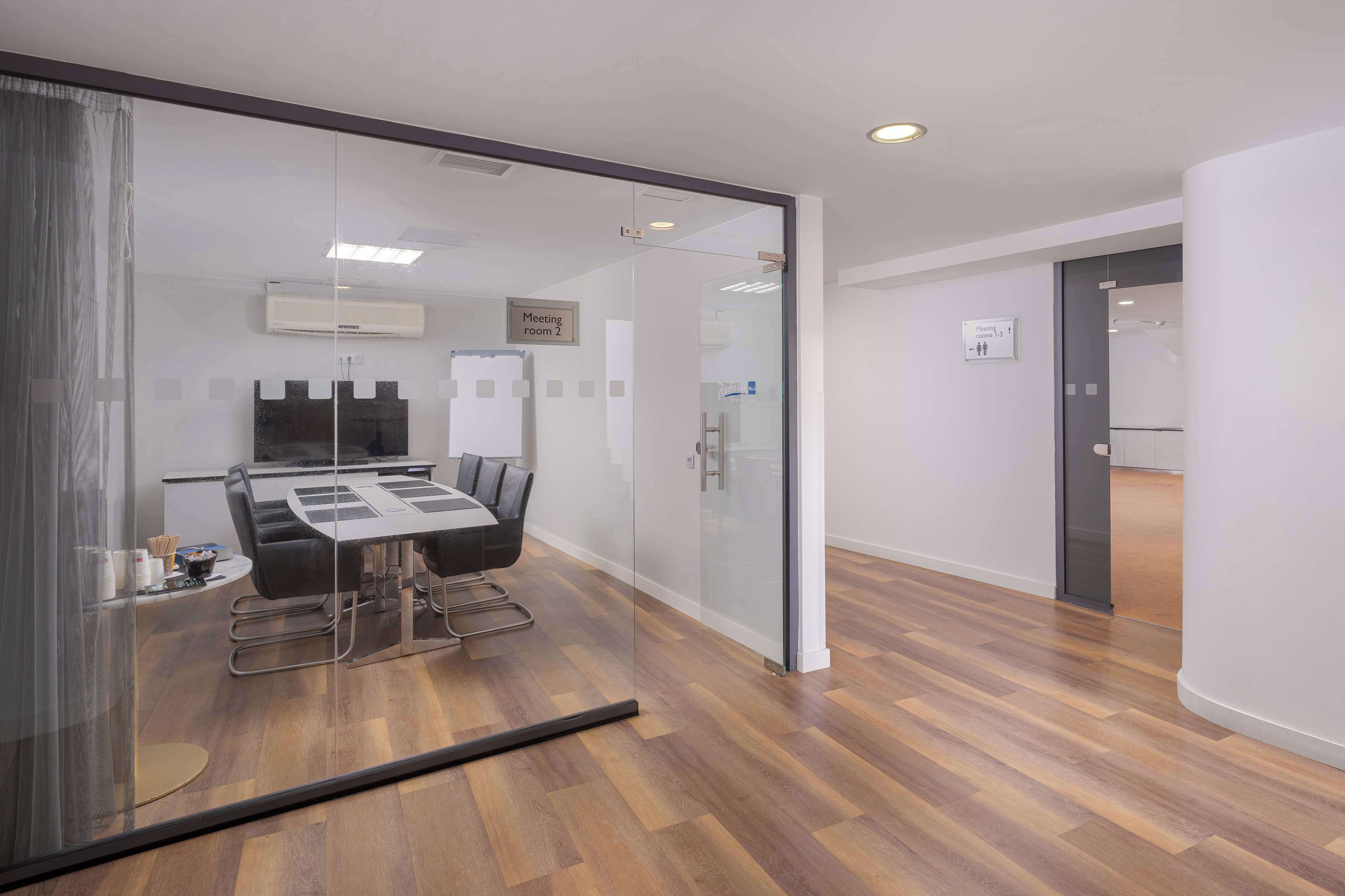 A modern meeting room with a glass partition, a conference table, and a black sofa.