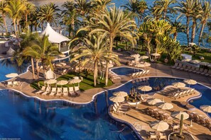 A resort with a large pool, palm trees, and lounge areas with umbrellas.