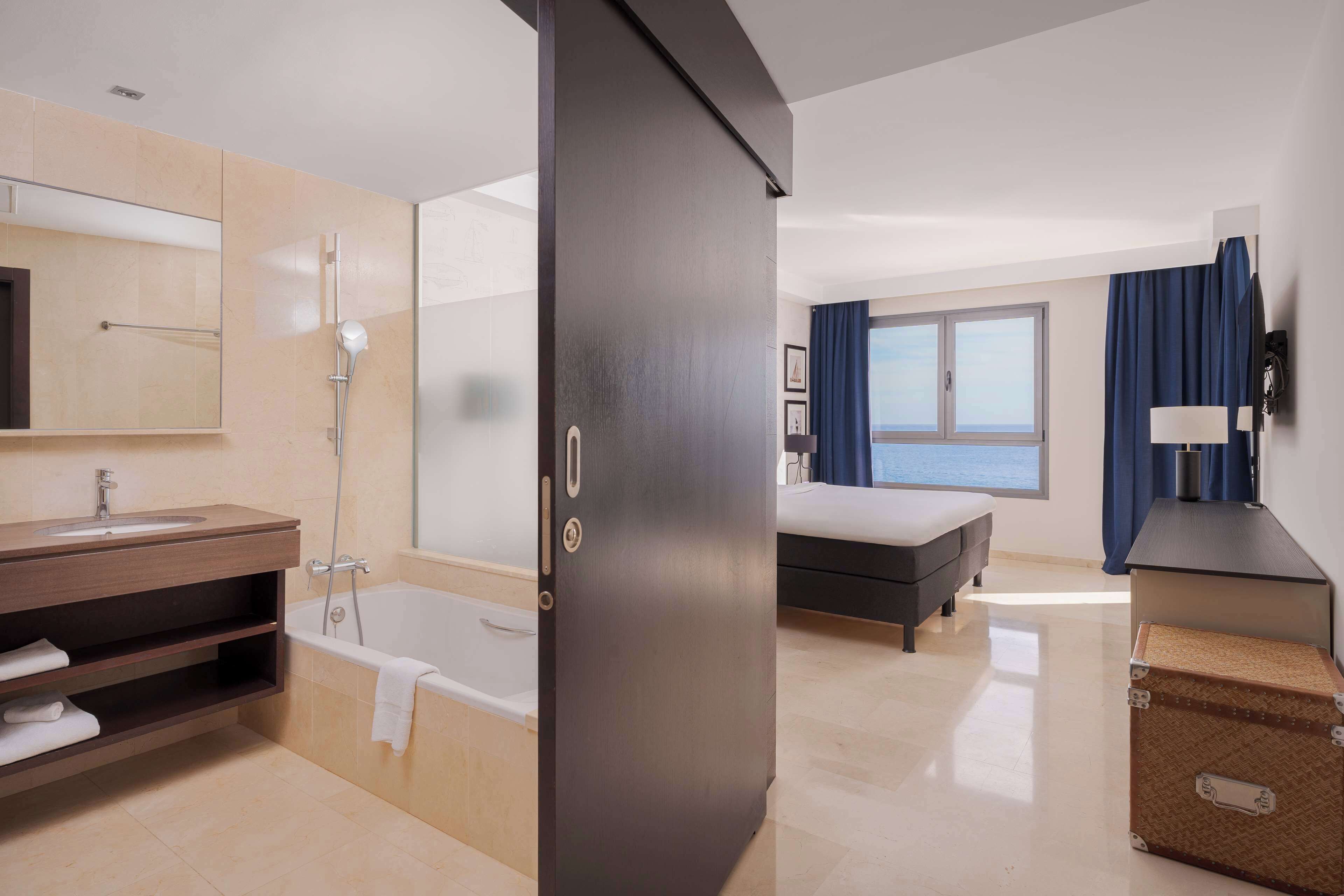 Habitación de hotel moderna con baño, cama, escritorio y vistas al mar.