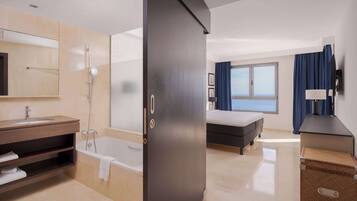 Habitación de hotel moderna con baño, cama, escritorio y vistas al mar.