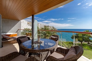 A balcony with wicker furniture, a glass table, and a view of the ocean and buildings. - Radisson Blu Resort, Gran Canaria (Mogan)